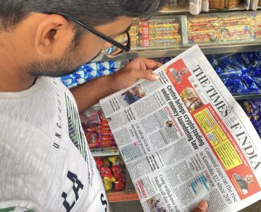 A person in India reading a newspaper about Government of India's notification under the PMLA, regulating virtual digital asset activities for businesses to prevent money laundering.