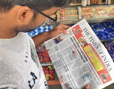 A person in India reading a newspaper about Government of India's notification under the PMLA, regulating virtual digital asset activities for businesses to prevent money laundering.